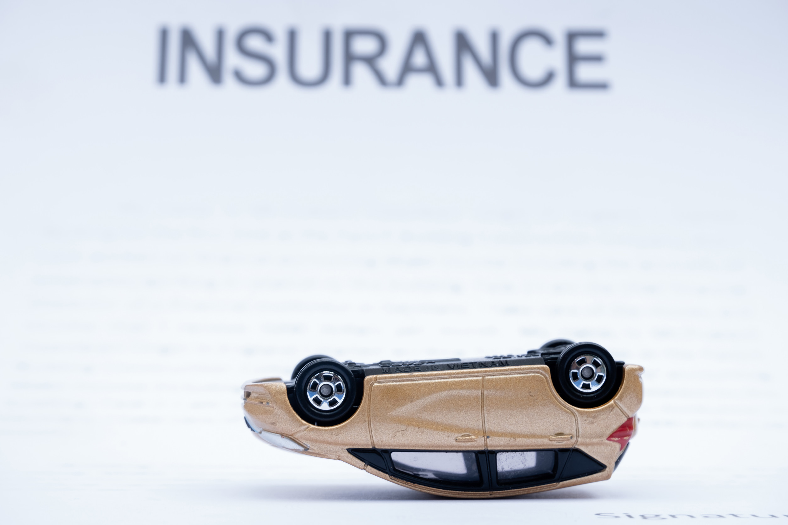 A toy car is flipped upside down in front of blurred text that reads 