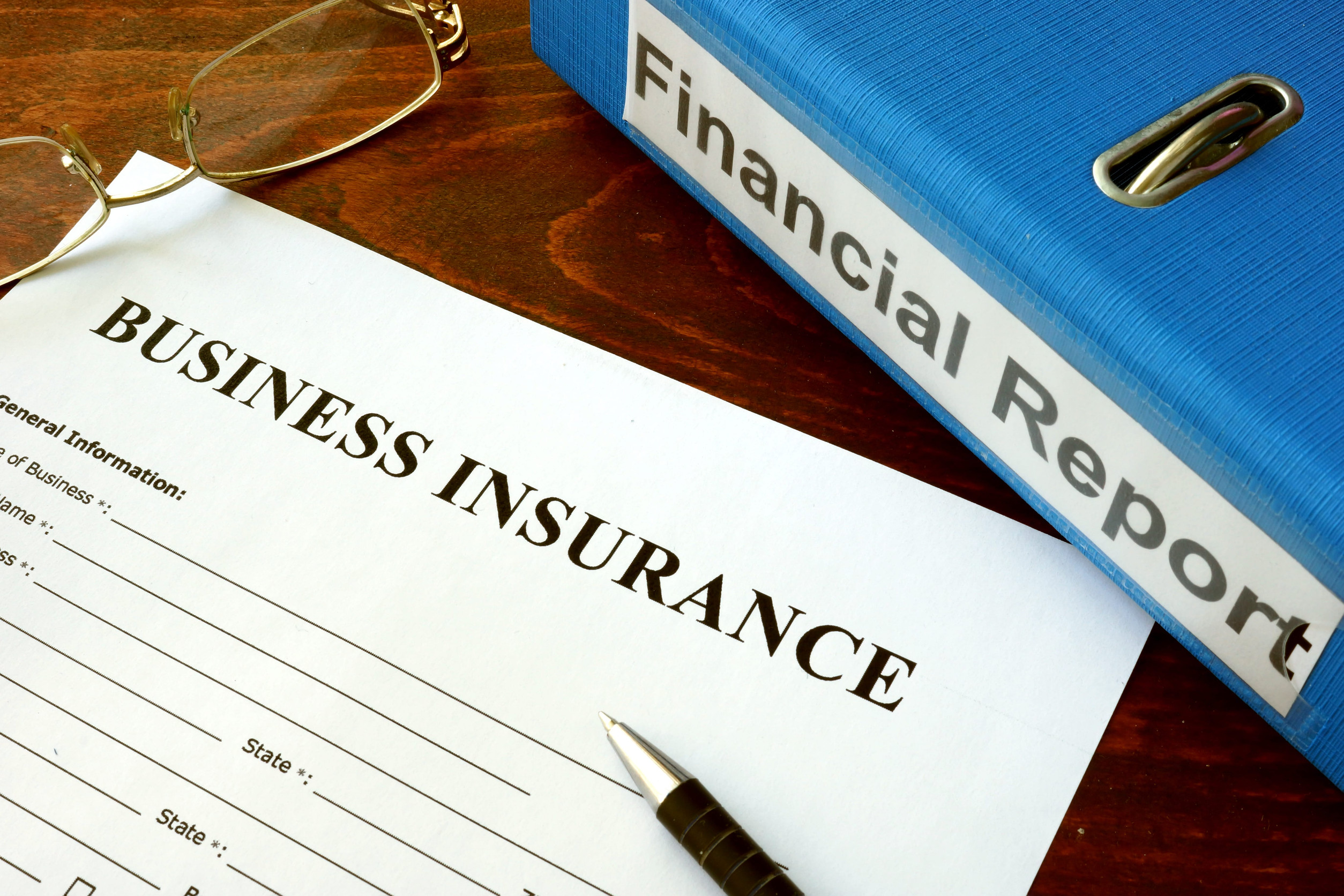 A business insurance coverage form with a pen, eyeglasses, and a blue binder labeled 